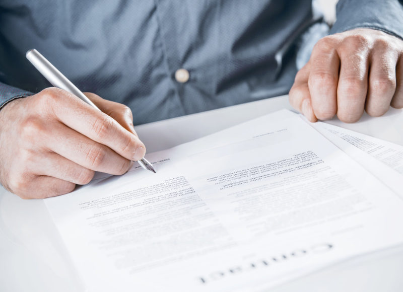 Businessman signing a legal document with text with a silver fountain pen, close up of his hands as he sits at a desk